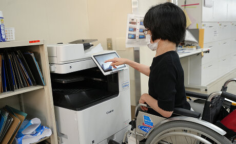 車いすに乗った社員が、コピー機のタッチパネルを操作している様子