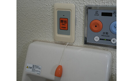 トイレの壁に設置された、「呼出 CALL PUSH」と書かれたオレンジ色の緊急呼び出しボタンと、その下に垂れた引きひも