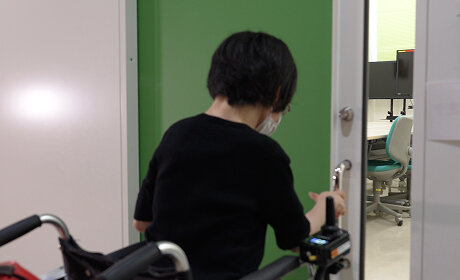 電動車いすに乗った社員が、緑色の引き戸の取手に手をかけて開けている様子