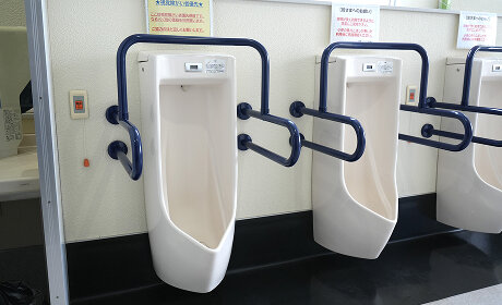 青い手すりが付いた小便器が並ぶ男子トイレ
